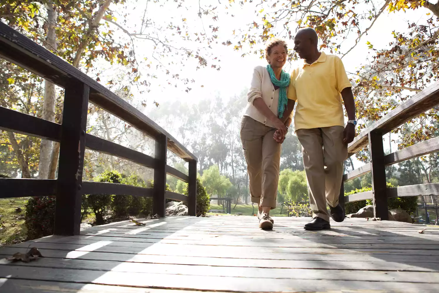 A couple takes a stroll across a bridge in a park.