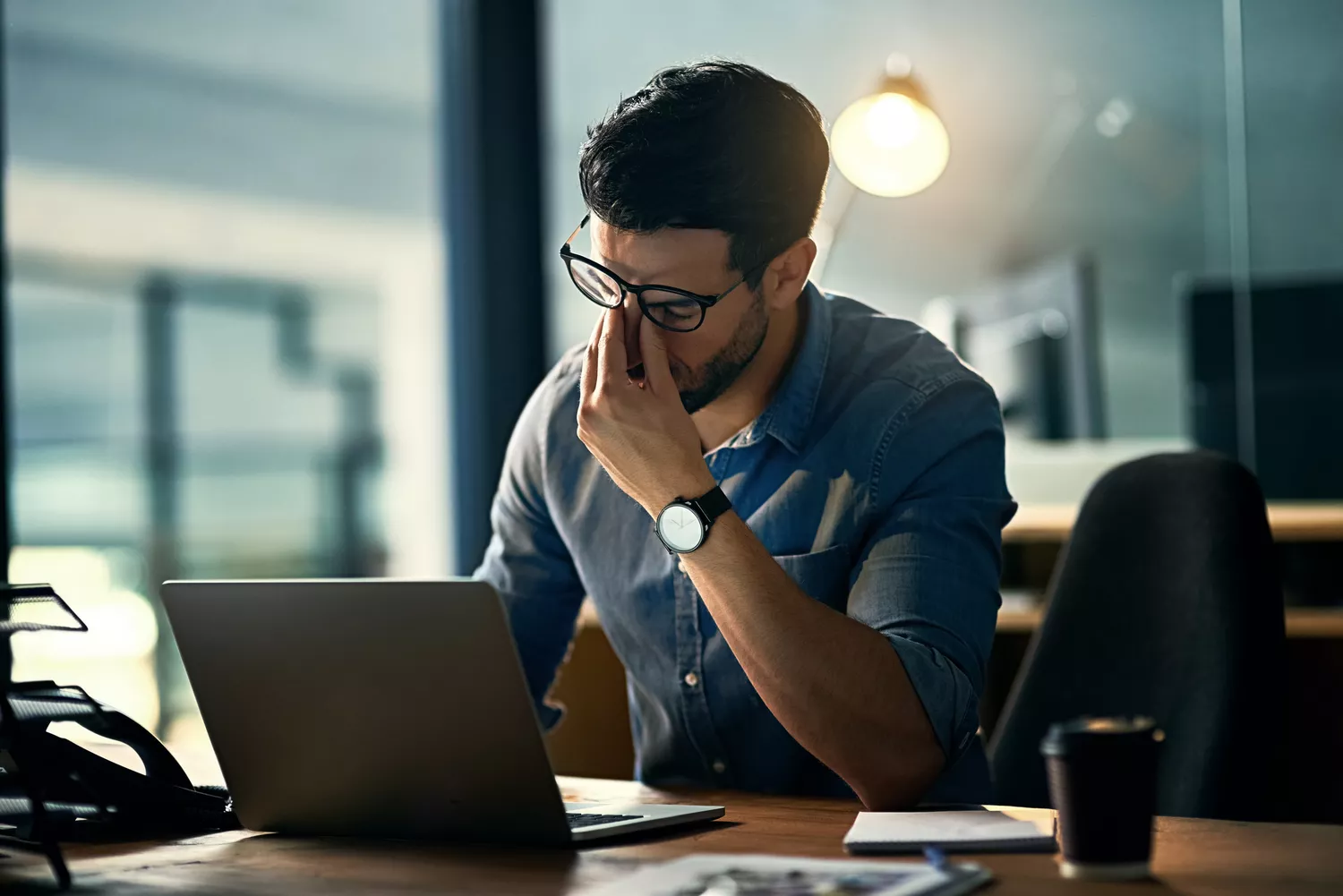 Man using laptop pinches bridge of nose and shuts eyes